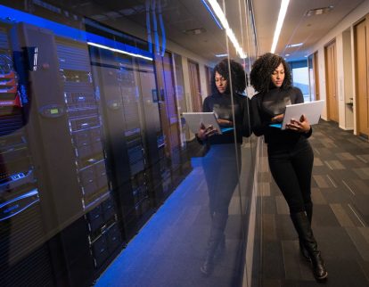 pexels-photo-1181316-1181316 A woman using a laptop navigating a contemporary data center with mirrored servers.